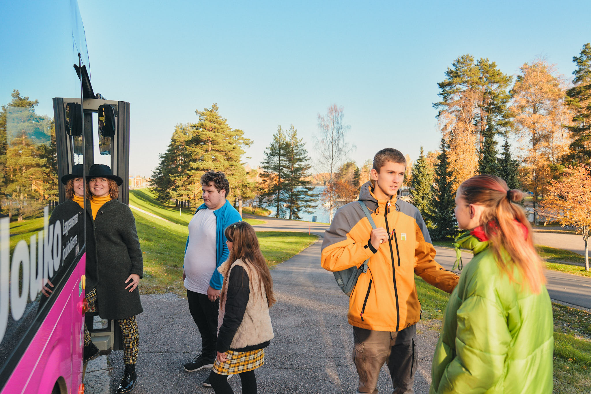 Joukko ihmisiä astumassa bussin kyytiin syksyisessä maisemassa.